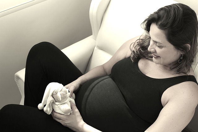 ginekolog szczecin - przyszła mama w zaawansowanej ciąży uśmiecha się do misia w oczekiwaniu na dziecko